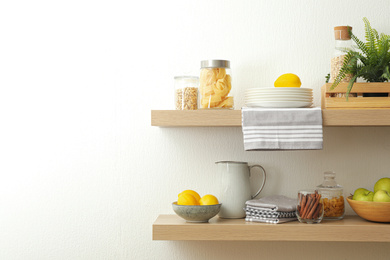 Photo of Wooden shelves with dishware and products on white wall. Kitchen interior idea