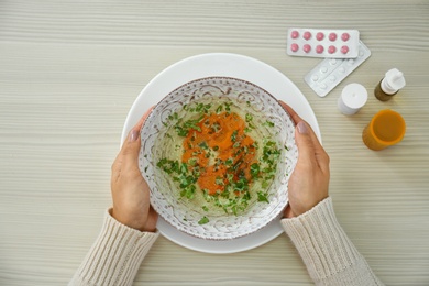 Photo of Woman with bowl of soup at wooden table, top view. Flu treatment