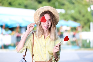 Beautiful smiling woman with candies showing her tongue on city street