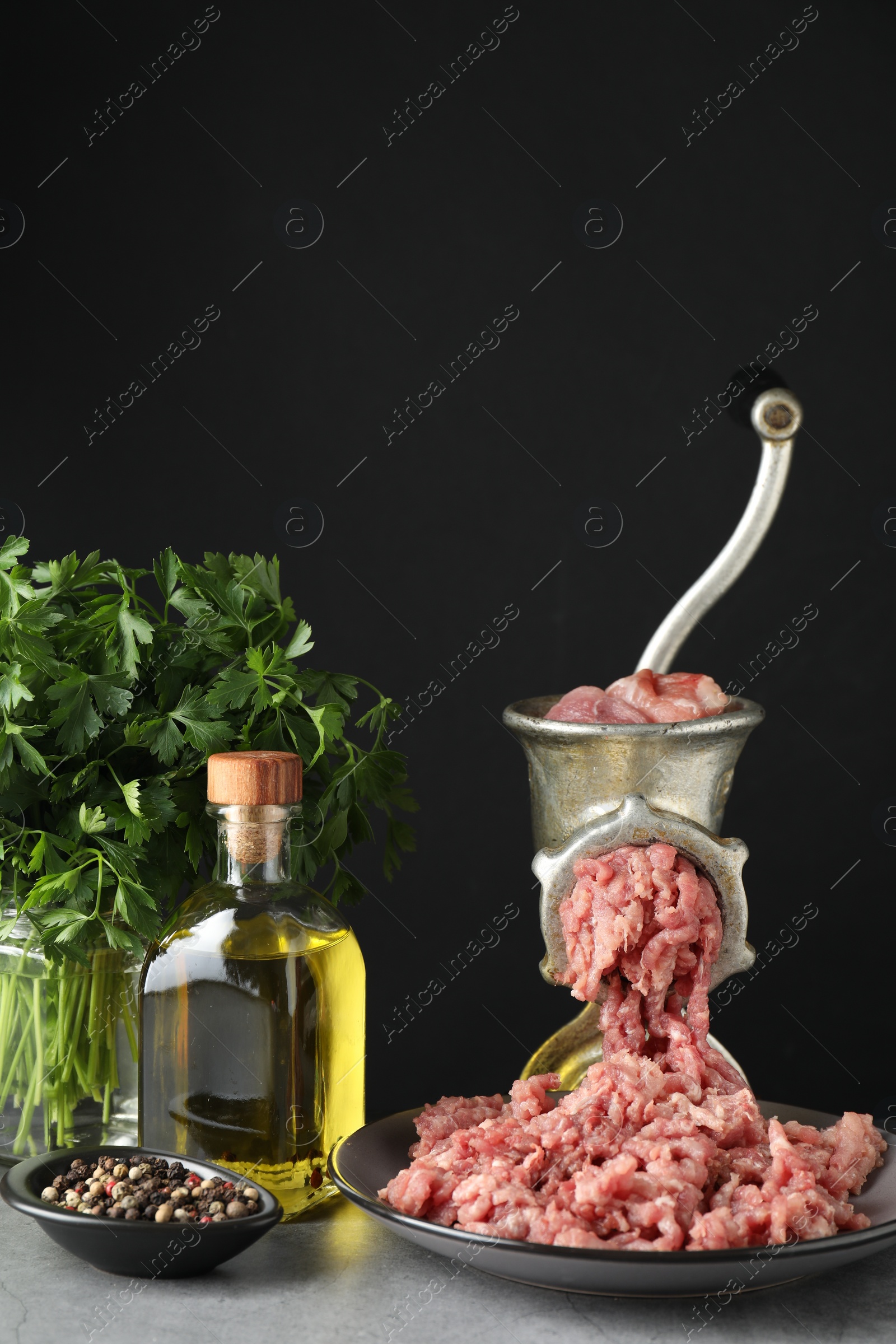 Photo of Manual meat grinder with beef mince, spices, oil and parsley on grey table