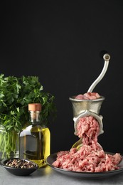 Manual meat grinder with beef mince, spices, oil and parsley on grey table