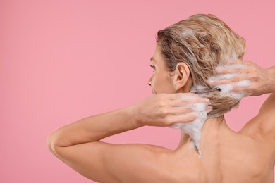 Photo of Woman washing hair on pink background, back view. Space for text