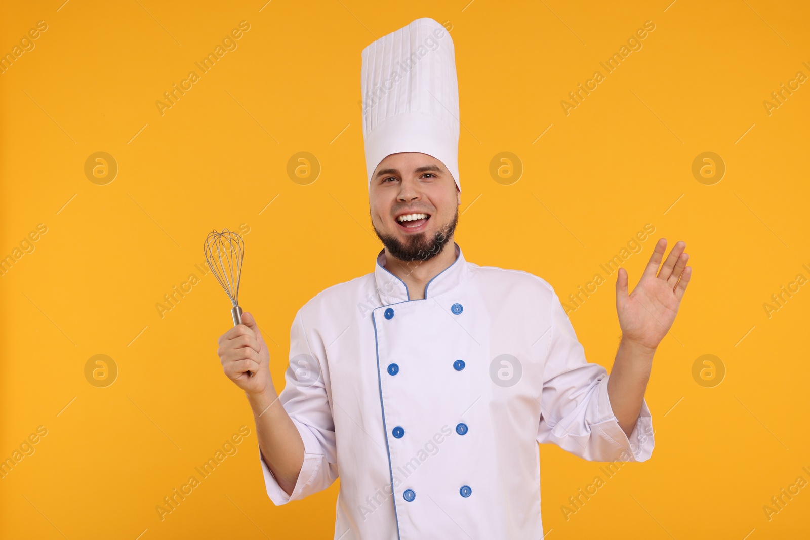 Photo of Happy professional confectioner in uniform holding whisk on yellow background