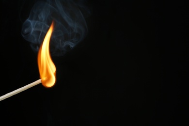 Burning matchstick on black background, closeup. Space for text