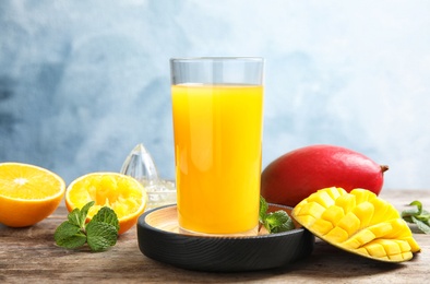 Photo of Glass of fresh mango drink and tropical fruits on table against color background