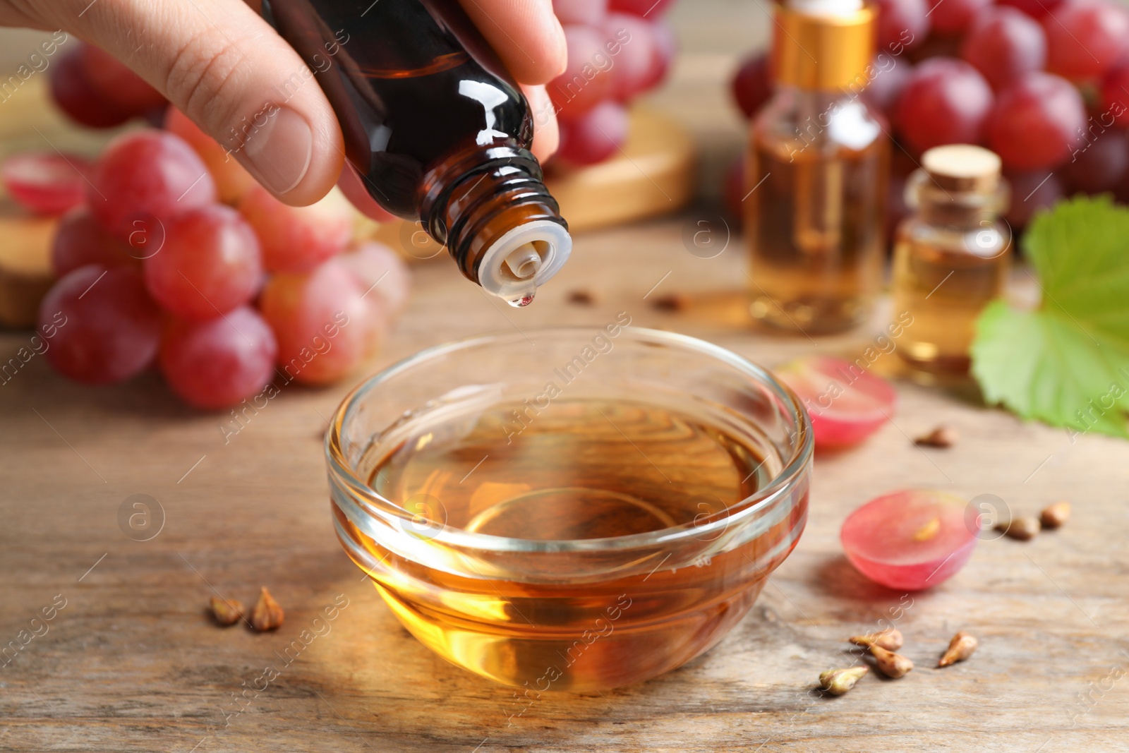 Photo of Woman dripping natural grape seed oil into bowl at wooden table, closeup. Organic cosmetic