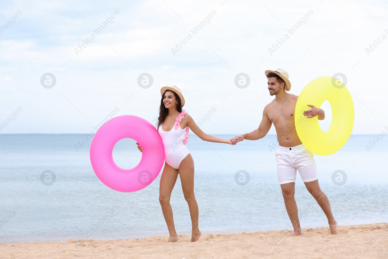 Photo of Happy young couple having fun with inflatable rings on beach near sea