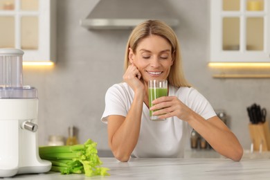 Photo of Woman with glass of fresh celery juice at table in kitchen