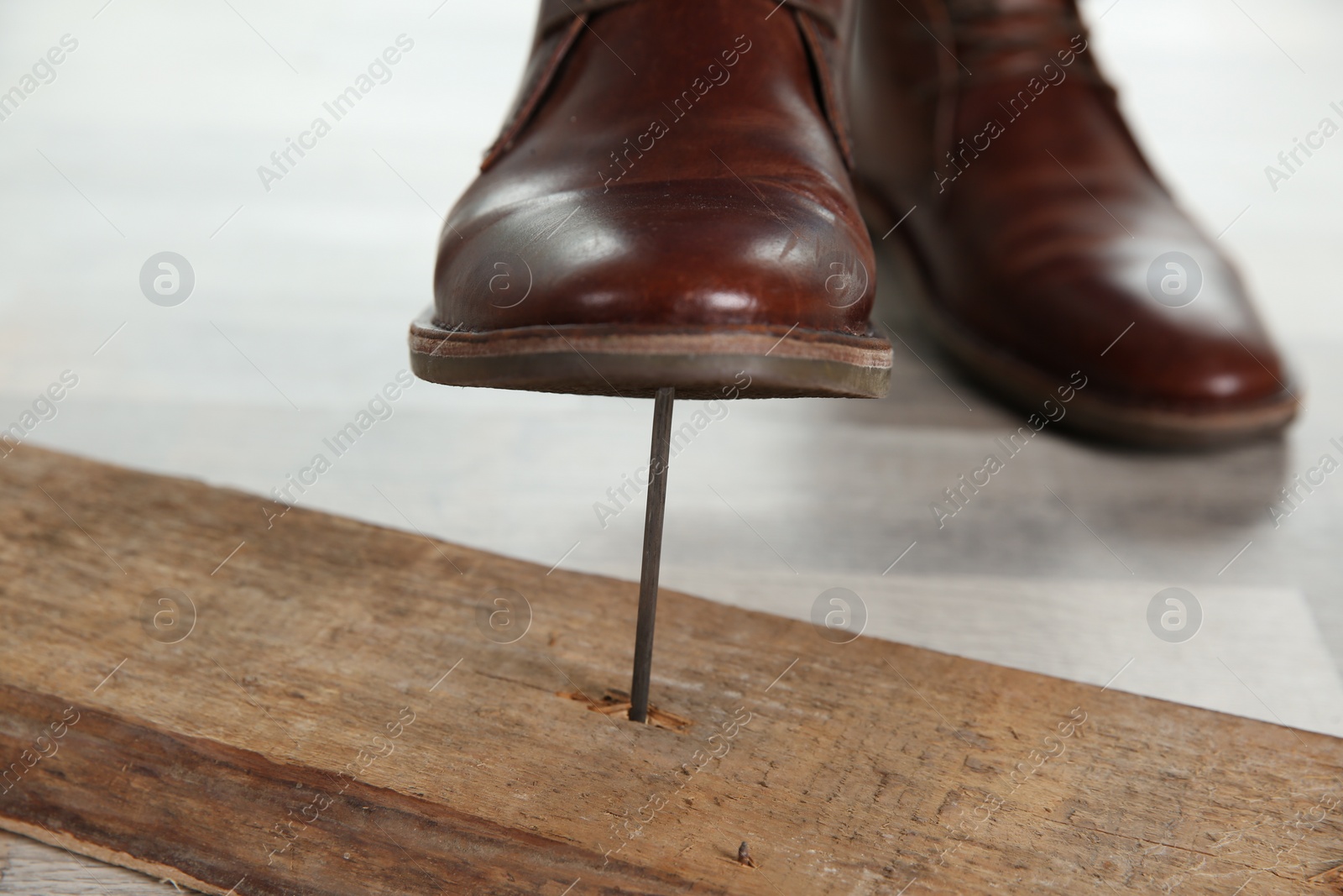 Photo of Careless man stepping on nail in wooden plank, closeup