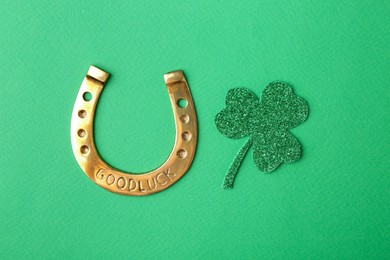 Photo of St. Patrick's day. Golden horseshoe and decorative clover leaf on green background, flat lay