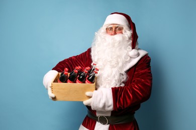 Photo of MYKOLAIV, UKRAINE - JANUARY 18, 2021: Santa Claus holding wooden crate full of Coca-Cola bottles on light blue background