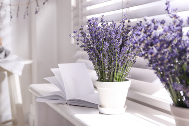 Photo of Beautiful lavender flowers and book on window sill indoors