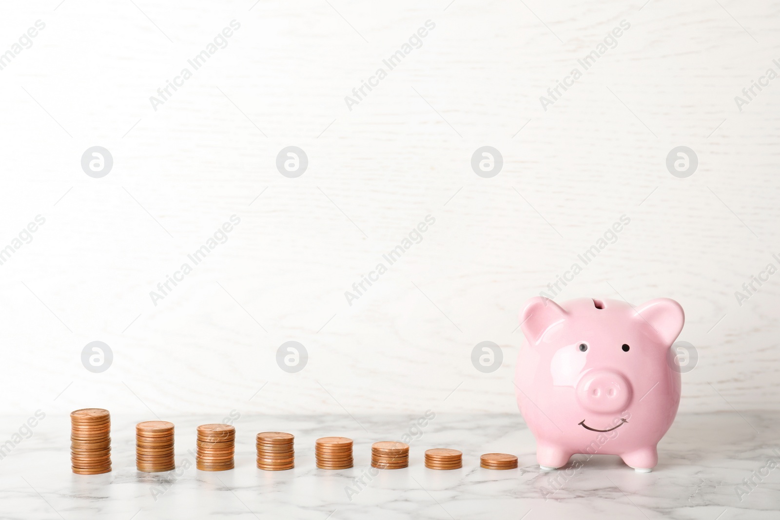 Photo of Piggy bank and different height coin stacks on table. Space for text