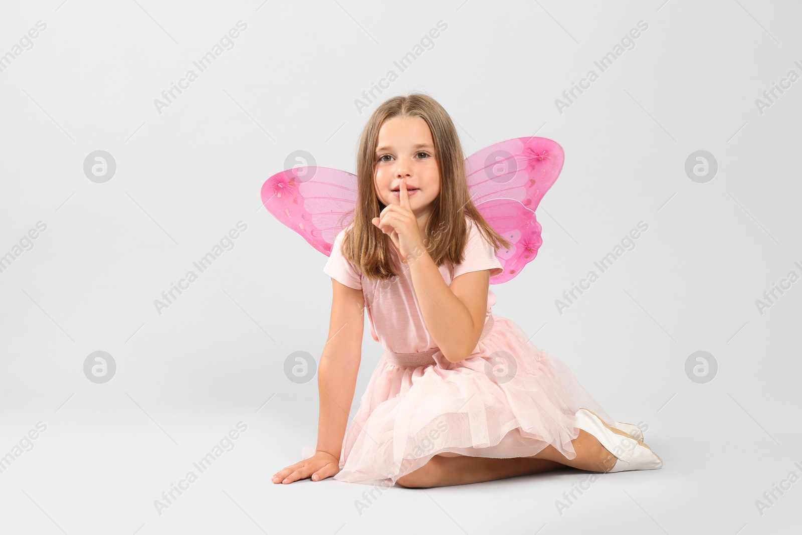 Photo of Cute little girl in fairy costume with pink wings on light background