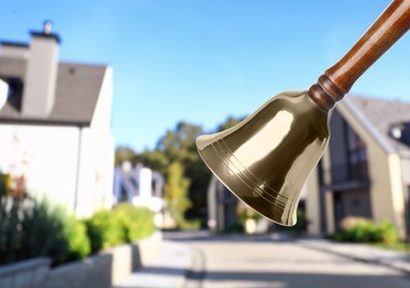 Image of Golden school bell with wooden handle and blurred view of street on sunny day