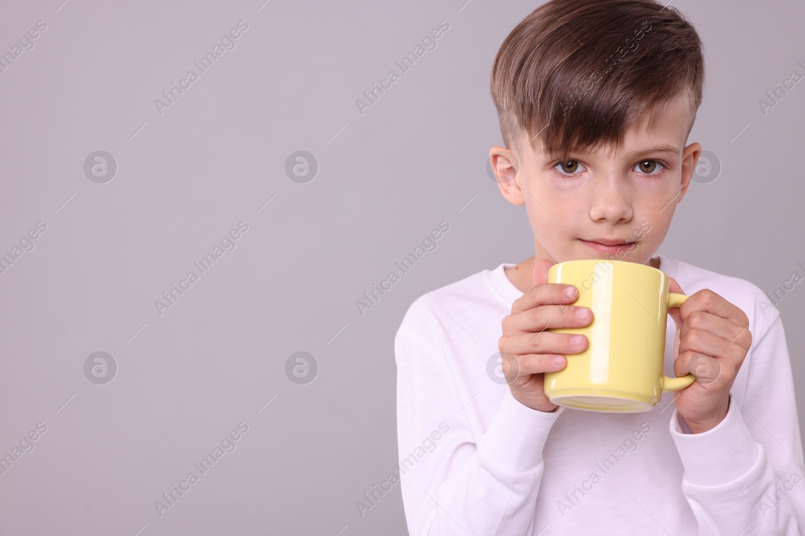 Photo of Cute boy with yellow ceramic mug on light grey background, space for text