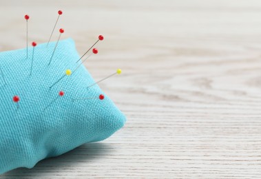 Photo of Light blue pincushion with sewing pins on wooden table, closeup. Space for text