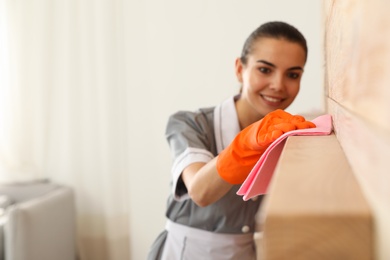 Photo of Young chambermaid wiping dust from furniture with rag in hotel room, closeup. Space for text