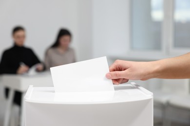 Photo of Woman putting her vote into ballot box on blurred background, closeup