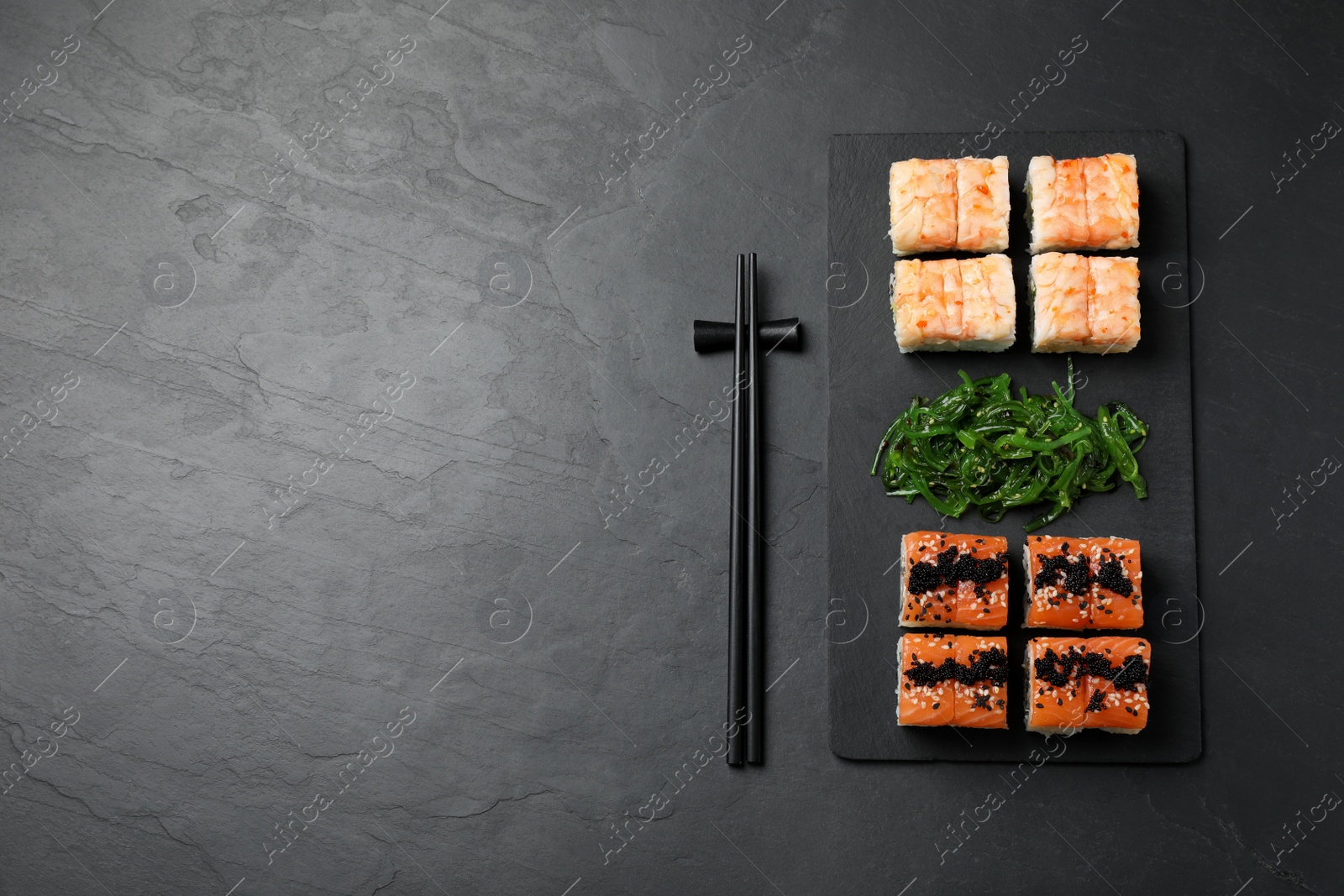 Photo of Delicious sushi rolls and chuka served on black table, flat lay. Space for text