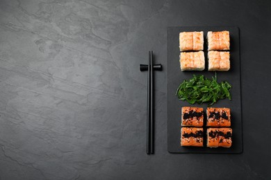 Photo of Delicious sushi rolls and chuka served on black table, flat lay. Space for text