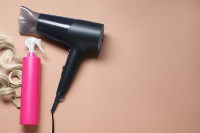 Photo of Spray bottle with thermal protection, lock of blonde hair and modern hairdryer on beige background, flat lay. Space for text