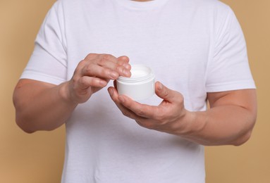 Photo of Man with jar of body cream on light brown background, closeup