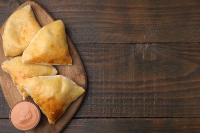 Photo of Delicious samosas and sauce on wooden table, top view. Space for text