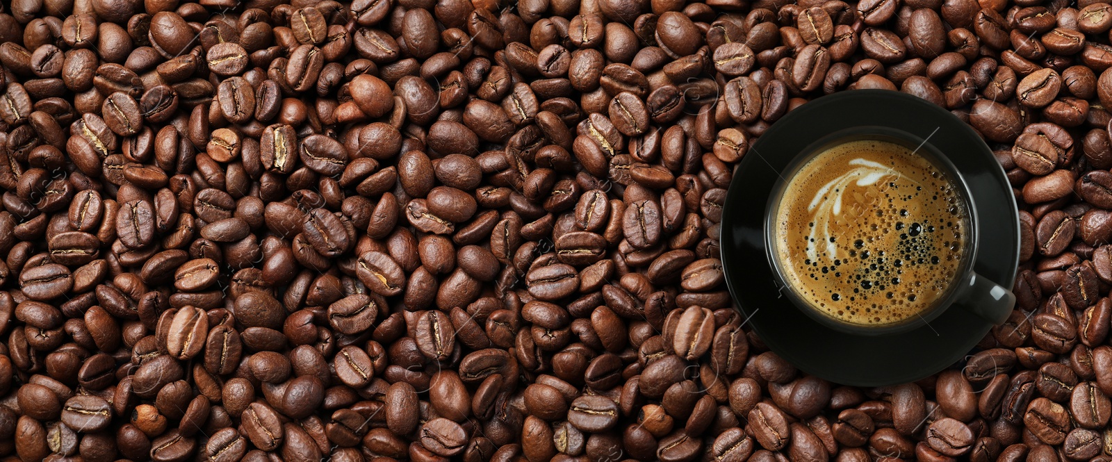 Image of Cup of tasty aromatic coffee on roasted beans, top view. Banner design