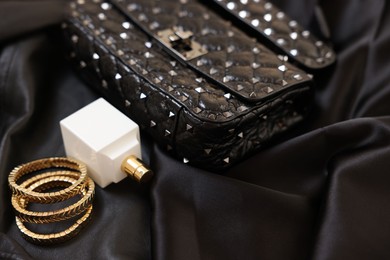 Leather bag, bottle of perfume and golden bracelets on black fabric, closeup