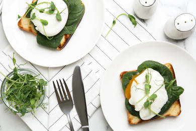 Delicious poached egg sandwiches served on white marble table, flat lay