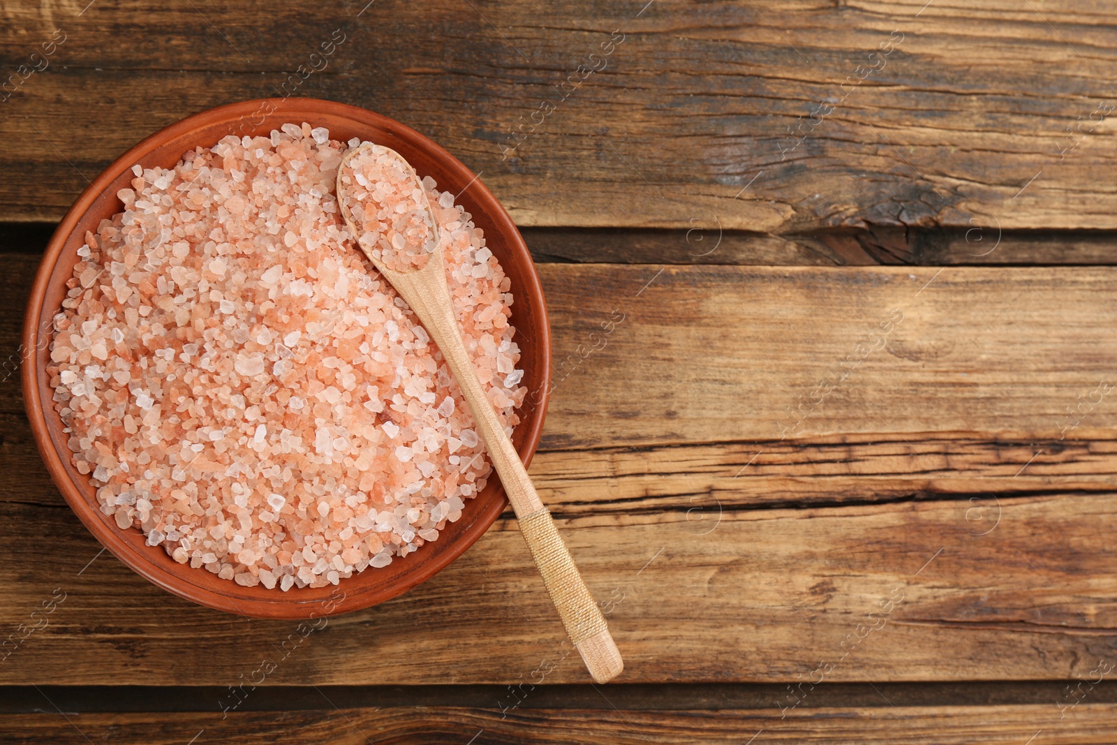 Photo of Bowl and spoon with pink himalayan salt on wooden table, top view. Space for text