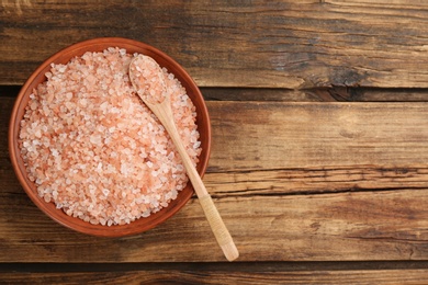 Bowl and spoon with pink himalayan salt on wooden table, top view. Space for text