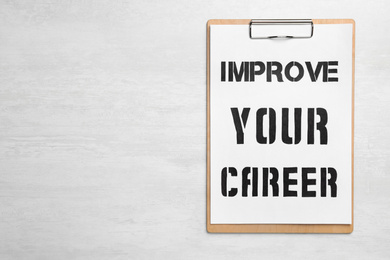 Photo of Clipboard with words IMPROVE YOUR CAREER on white wooden background, top view. Space for text