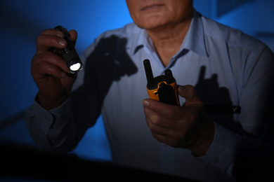 Photo of Professional security guard with portable radio set and flashlight in dark room, closeup