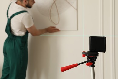 Photo of Cross line laser level and handyman hanging picture on white wall