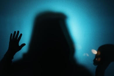 Photo of Silhouette of ghost behind glass against blue background