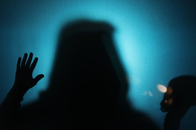 Silhouette of ghost behind glass against blue background