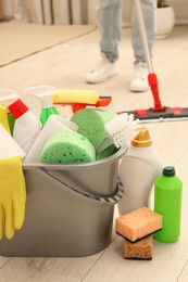 Photo of Different cleaning supplies in bucket and woman mopping floor, selective focus