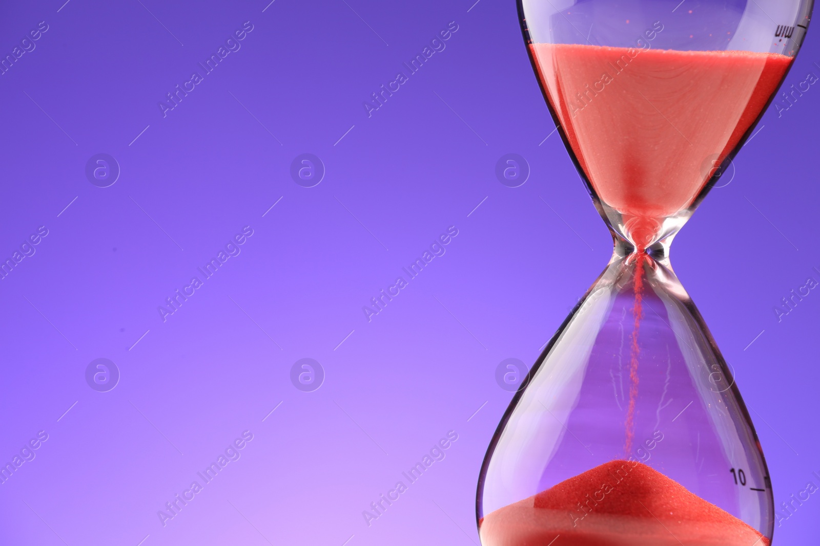 Photo of Hourglass with red flowing sand on purple background, closeup. Space for text