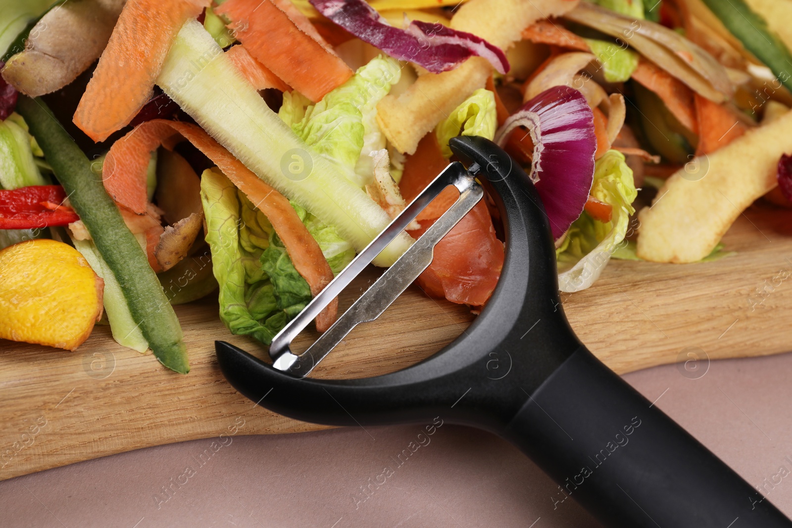 Photo of Peels of fresh vegetables and peeler on dusty pink background, closeup