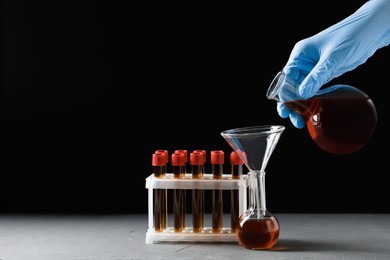Photo of Scientist pouring brown liquid into flask at grey table against black background, closeup. Space for text