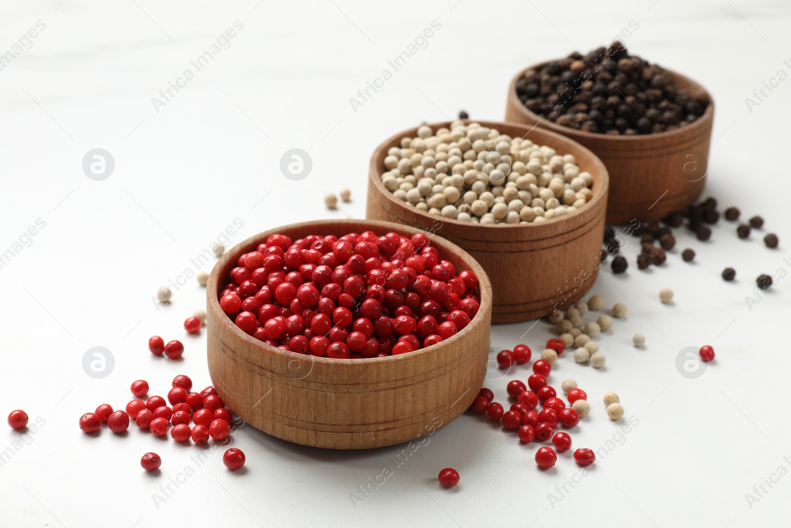 Photo of Aromatic spice. Different peppers in bowls on white table, closeup