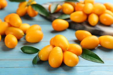Photo of Fresh ripe kumquats and leaves on light blue wooden table, closeup