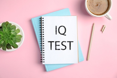 Notebook with text IQ Test, pen, plant and cup of coffee on pink background, flat lay