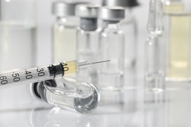 Photo of Glass vial and syringe with medication on white table, closeup. Space for text