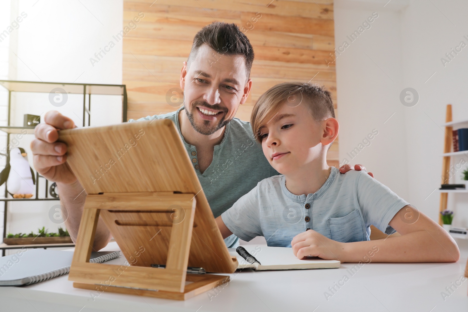 Photo of Boy with father doing homework using tablet at table indoors