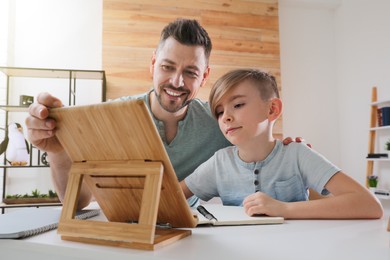 Photo of Boy with father doing homework using tablet at table indoors