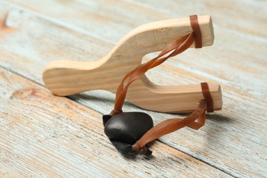 Photo of Slingshot with pebble on light blue wooden table, closeup