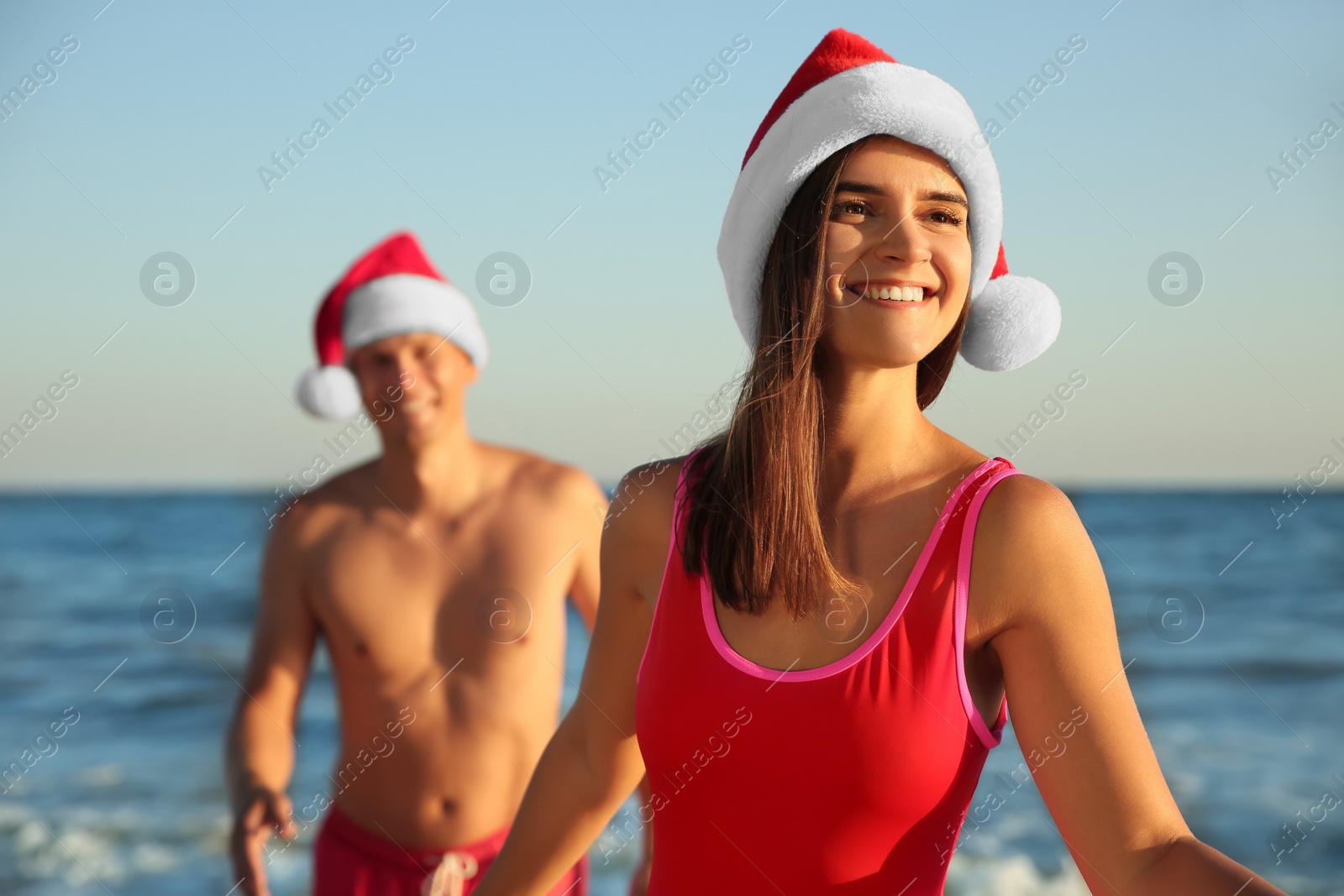 Photo of Happy couple with Santa hats together on beach. Christmas vacation